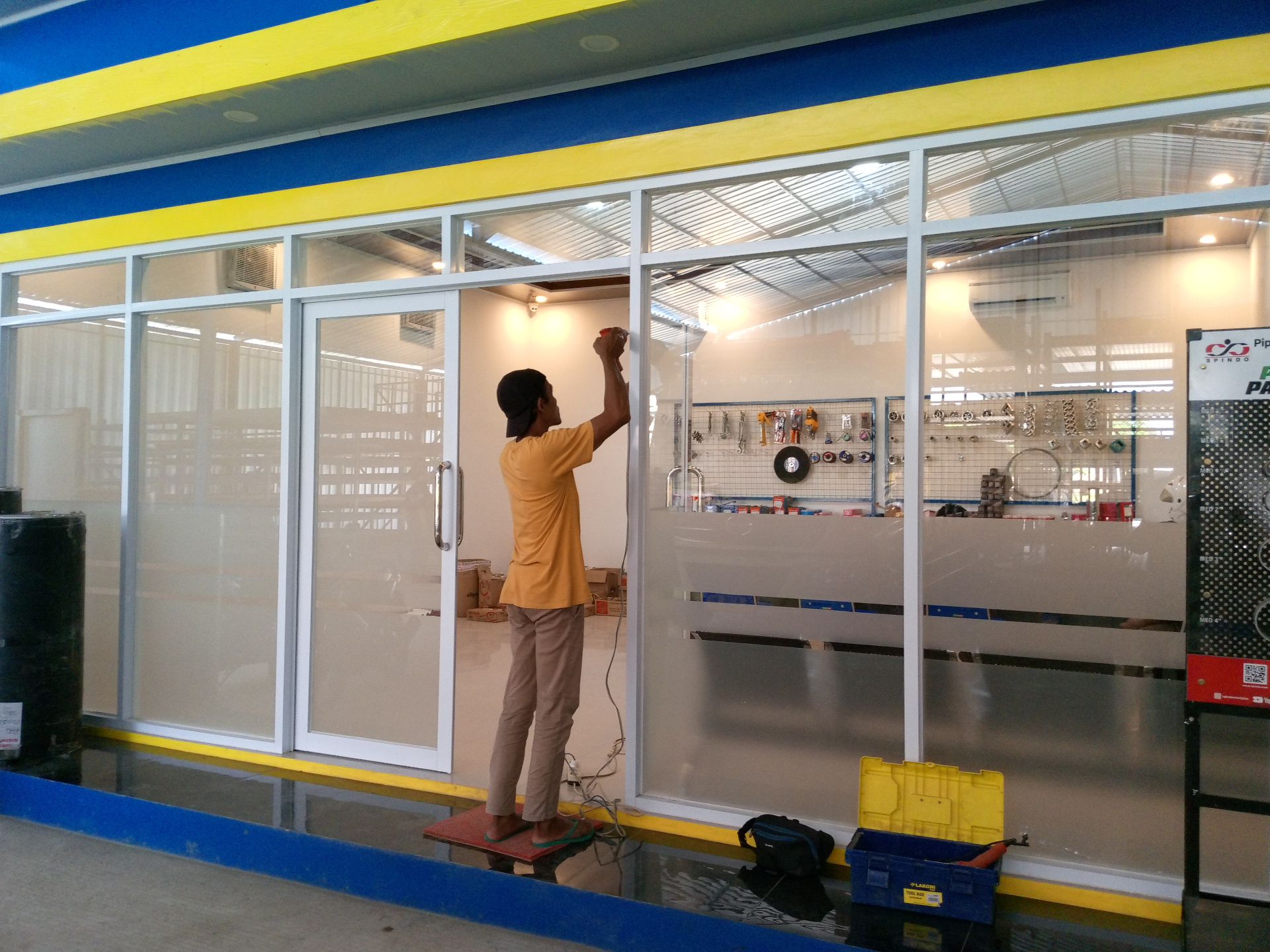 Proses pemasangan partisi aluminium kaca dengan pintu sliding di area toko